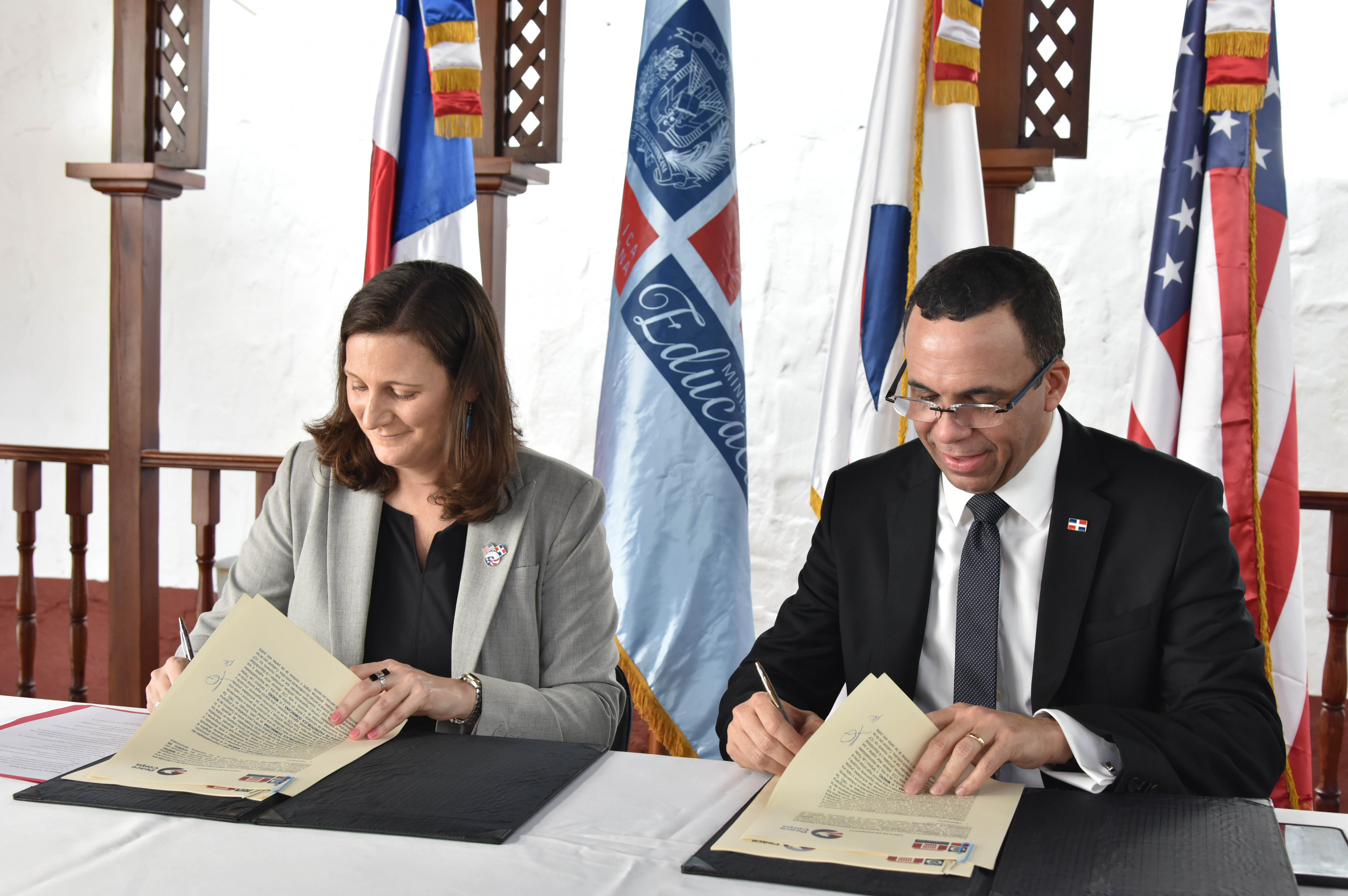  imagen Ministro Andrés Navarro y la representante del Cuerpo de Paz de Estados Unidos, Kristin Kaper sentados firmando acuerdo de entendimiento para llevar voluntarios a las escuelas.  