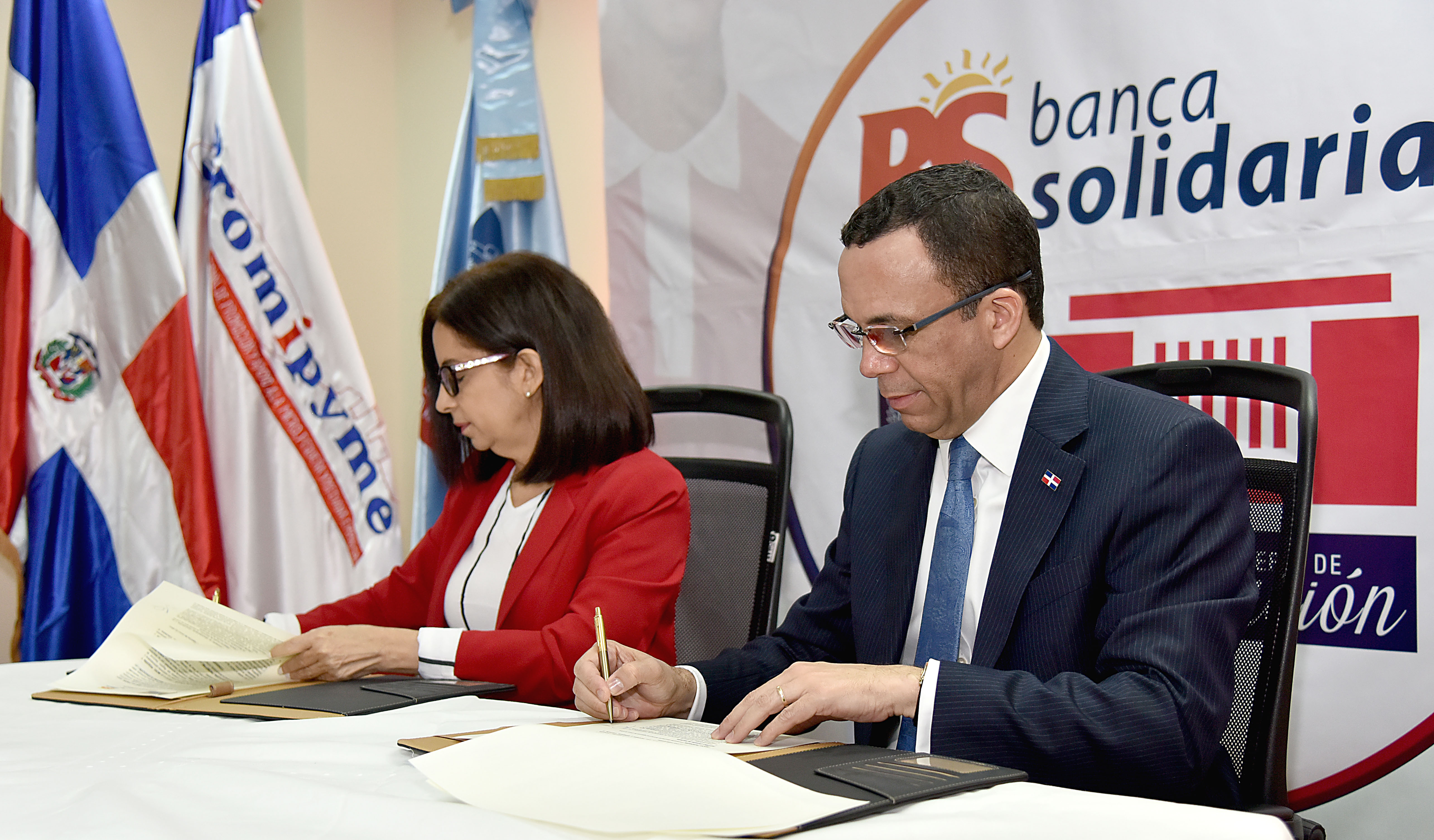  imagen Ministro Andrés Navarro y directora de Banca, Solidaria Maira Jiménez Pérez sentados firmando acuerdo interinstitucional  