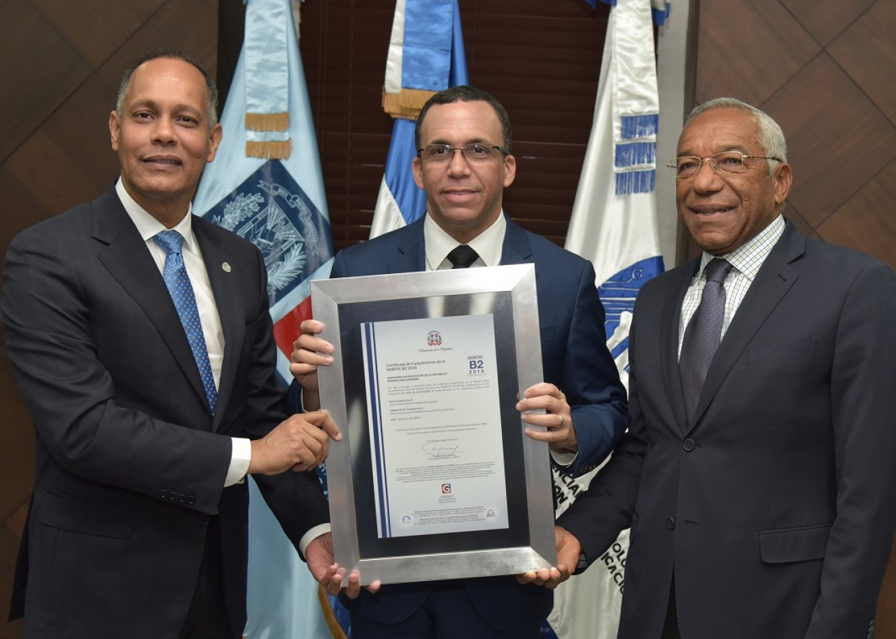  imagen Ministro Andrés Navarro de pie sosteniendo certificación Nortic B2 de manos del Director de la OPTIC, Armando García y Magino Corporán de CONADIS. 