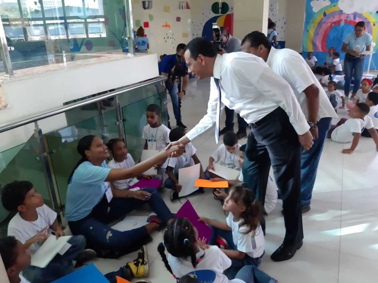 imagen Ministro de Educación saluda a facilitadora sentada en el piso junto a grupo de niños. 