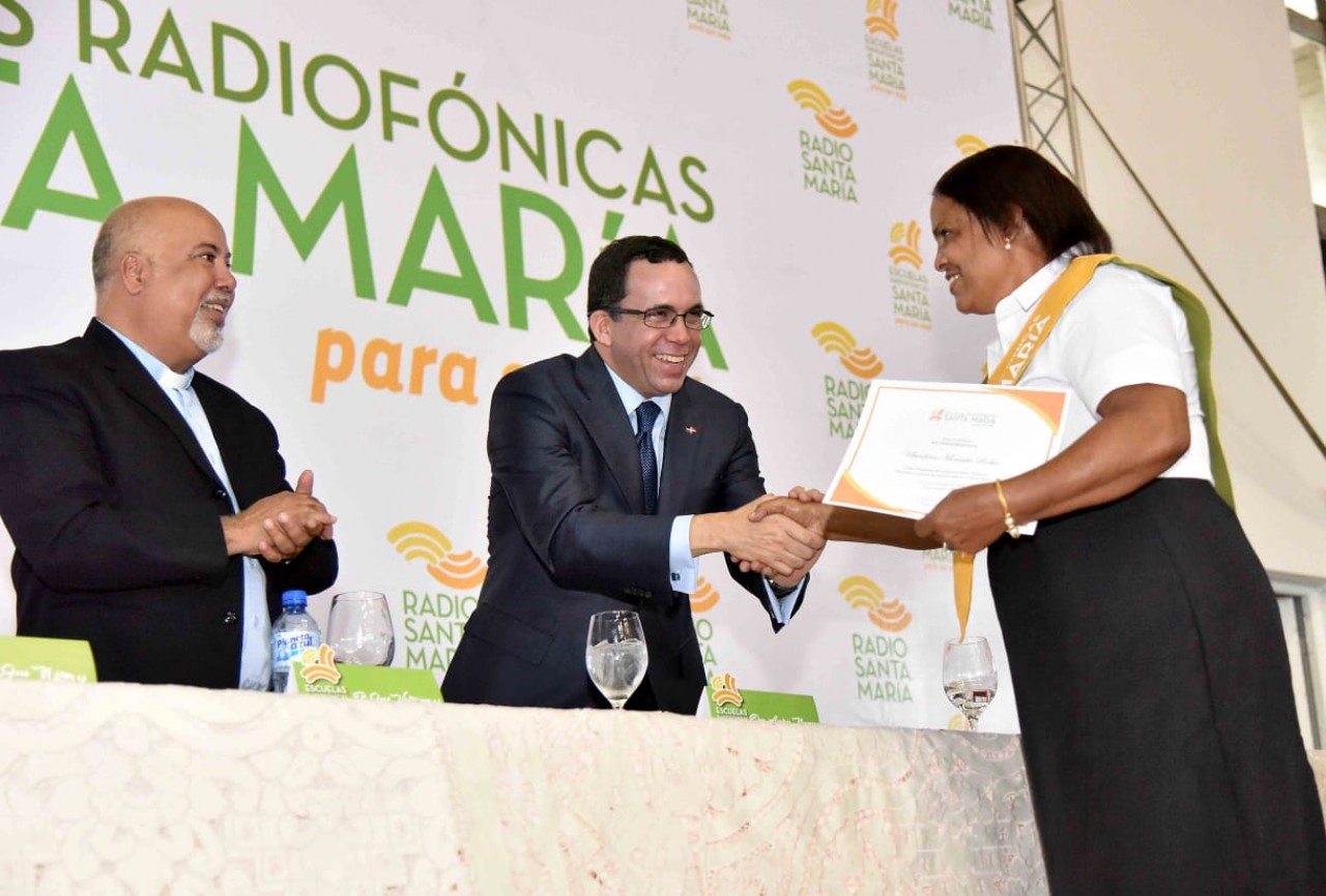  imagen Ministro Andrés Navarro desde mesa principal parado dándole la mano a una graduando de la Escuela Radiofónica  