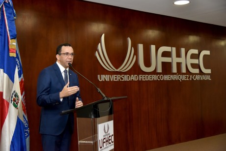  imagen Ministro AndrÃ©s Navarro de pie en podium dirigiendo discurso a personas en auditorium de la universidad Federico HenrÃ­quez y CarvajalÂ  